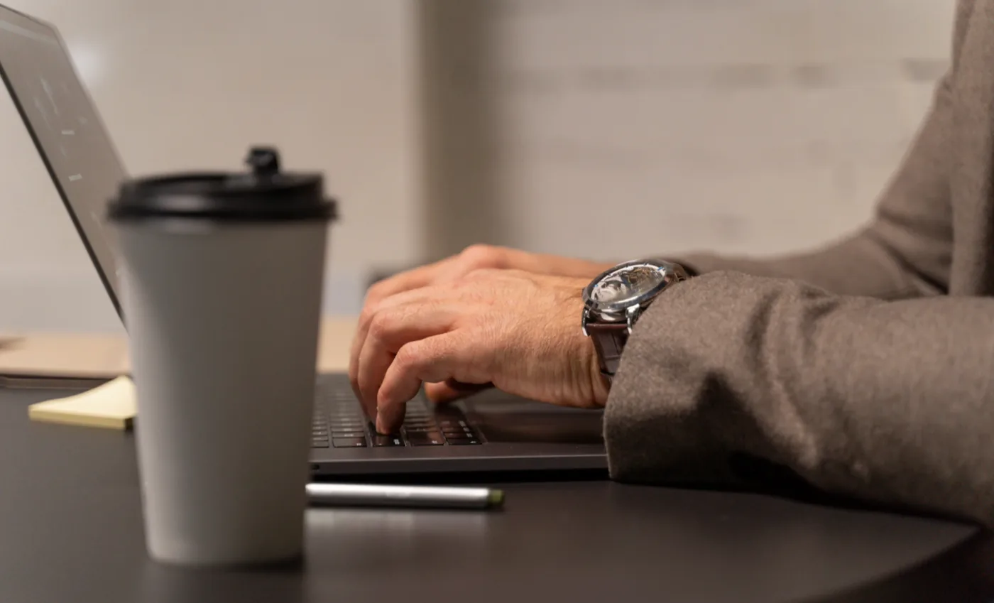 Mãos digitando em um notebook ao lado de um copo de café, representando o trabalho do dia a dia após a configuração